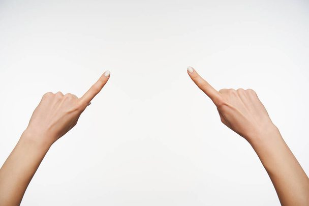 Foto horizontal de las manos de la señora mostrando en un punto con los dedos índice elevados mientras posando sobre fondo blanco. Mujeres mostrando la mano con lenguaje de señas
 - Foto, imagen