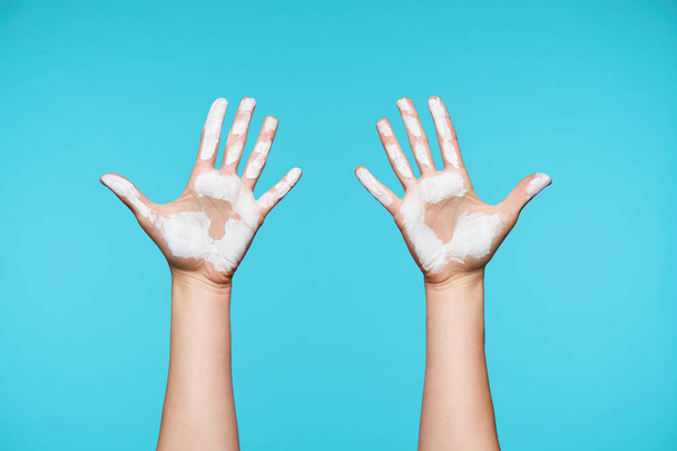 Studio photo of dirty raised woman's hand with white paint on it isolated against blue background, all fingers being separately from each other - Photo, Image
