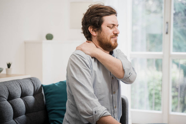 Painful guy aching from pain in back or neck at home - Photo, Image