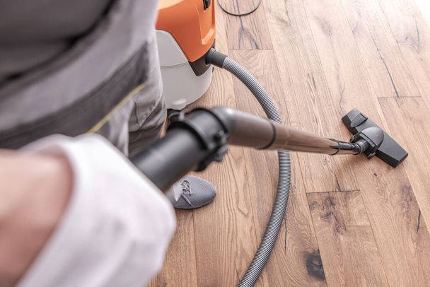 Close-up van de mens reinigen en stofzuigen hardhouten vloer na installatie van vloeren.  - Foto, afbeelding
