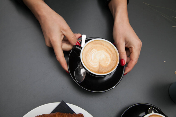 Cappuccino with the hand of women  and croissant in the black table  - Photo, Image
