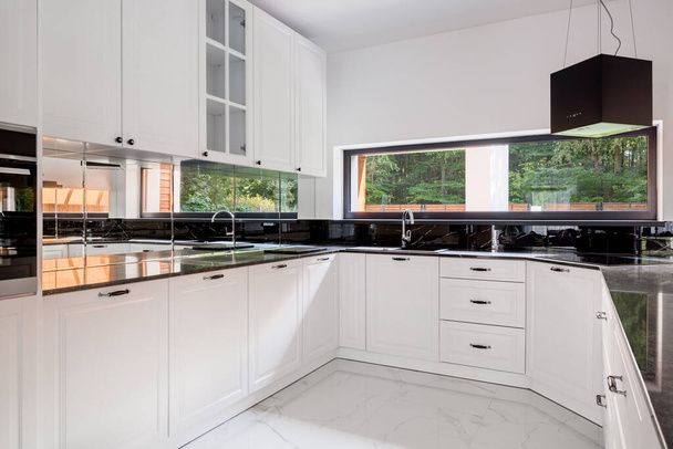Elegante Kücheneinrichtung mit Fenster, weißem Boden und Möbeln und schwarzen Arbeitsplatten - Foto, Bild