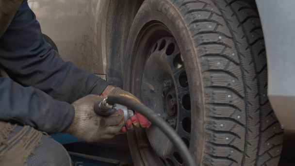 Naht die Hände des Arbeiters mit automatischen Schraubendrehschrauben am Autorad. Auto-Radwechsel in einer Kfz-Werkstatt - Foto, Bild