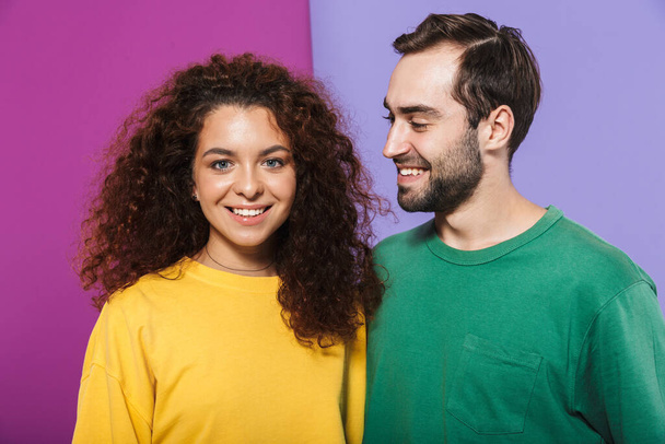 Portrait of brunette caucasian couple in colorful clothing smiling together, man looking at woman isolated over violet background - Фото, зображення