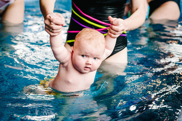 Young mother, swimming instructor and happy little girl in paddling pool. Teaches infant child to swim. Enjoy first day of swimming in water. Mom holds hand child preparing for diving. doing exercises - Photo, Image