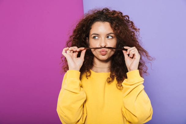 Image of beautiful happy curly woman swearing casual clothes smiling and having fun with her hair isolated over purple background - Fotografie, Obrázek