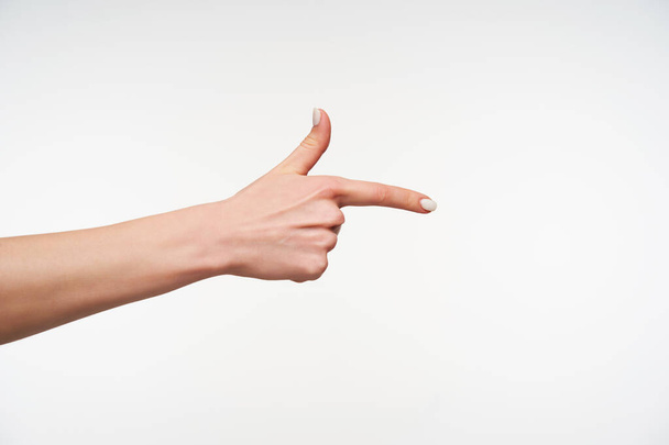 Photo of young woman's hand with white manicure being raised while showing aside with raised forefinger, isolated against white background - Photo, Image