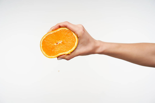 Alza la mano della giovane bella donna dalla pelle chiara tenendo metà arancione e premendola con le dita mentre viene isolata su uno sfondo bianco
 - Foto, immagini