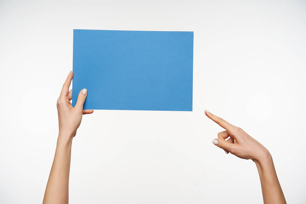 Horizontaal schot van het kwadraat van blauw papier wordt gehouden door de handen van jonge vrouw met witte manicure terwijl wordt geïsoleerd over witte achtergrond - Foto, afbeelding