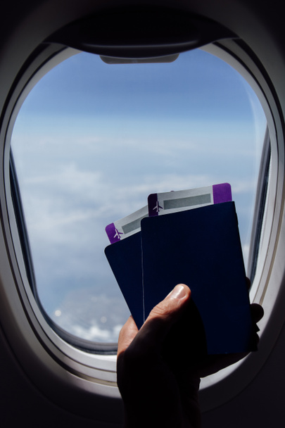 Vista recortada del hombre sosteniendo pasaportes con tarjetas de embarque cerca de ojo de buey en avión
  - Foto, imagen