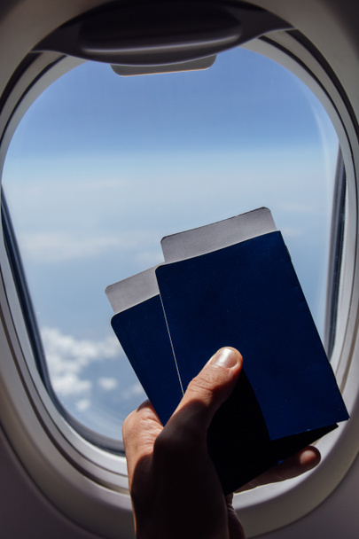 Cropped view of man holding in hand passports with air tickets near airplane porthole - Photo, Image