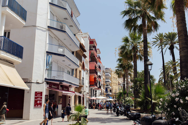 CATALONIA, SPAIN - APRIL 30, 2020: People walking on urban street with palm trees and outdoor cafe  - 写真・画像