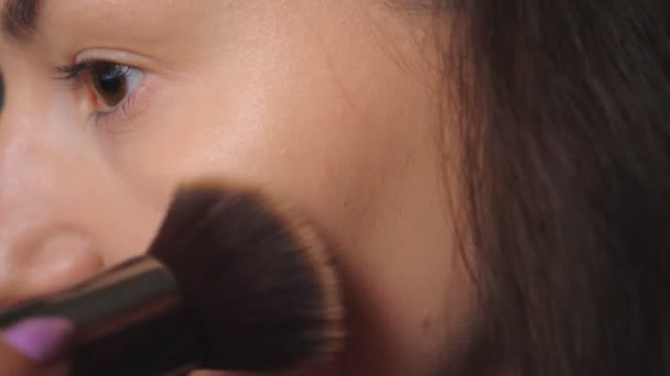 Young woman applying cosmetic on face using big brush. Pretty brunette caring about herself doing makeup. Attractive model in beauty salon. Concept of fashion and style. Detail view Close up - Séquence, vidéo