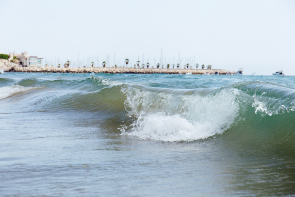 A tengerparti hullámok szelektív fókusza mólóval és pálmafákkal a háttérben, Katalónia, Spanyolország  - Fotó, kép