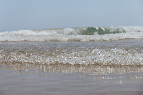 Selektywne skupienie fali na mokrej piaszczystej plaży z błękitnym niebem na tle - Zdjęcie, obraz