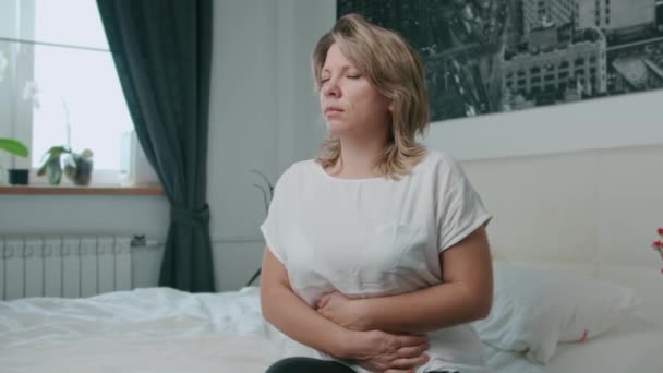 The woman has a stomachache. Sitting on the bed and held his hands - Imágenes, Vídeo