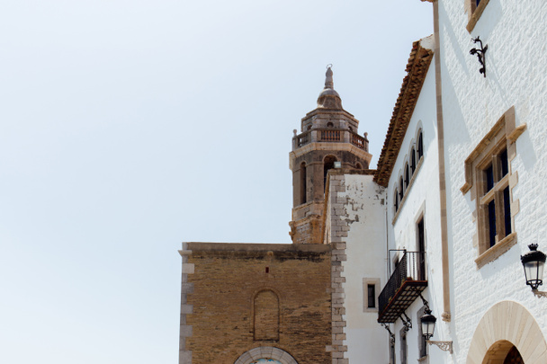 Vista en ángulo bajo de fachadas de casa e iglesia de San Bartolomé y Santa Tecla con cielo despejado al fondo en Barcelona, España
  - Foto, Imagen