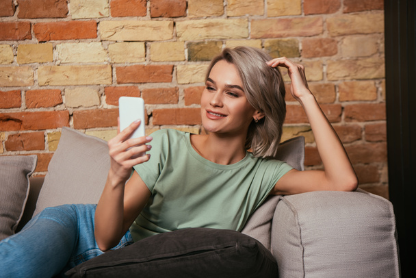happy young woman touching hair during video call on smartphone - Photo, Image