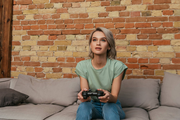 KYIV, UKRAINE - APRIL 30, 2020: focused young woman playing video game with joystick at home - Foto, imagen