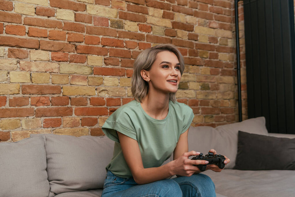 KYIV, UKRAINE - APRIL 30, 2020: excited girl playing video game with joystick at home - Foto, imagen