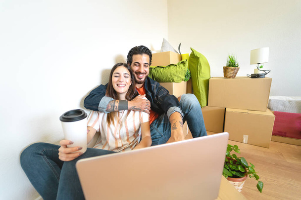 Happy young couple moving in new home first time - Man and woman having fun using computer next carton box in new property house - Change apartment day and people lifestyle relationship concept - Фото, изображение