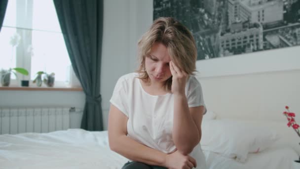 The woman has a headache. She sits on bed and holds her hands - Imágenes, Vídeo