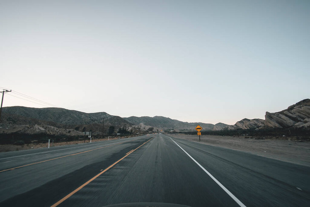 Пустое шоссе в Калифорнии Сразу после заката с желтой дорожной надписью и горами вдалеке во время пандемии коронавируса
 - Фото, изображение