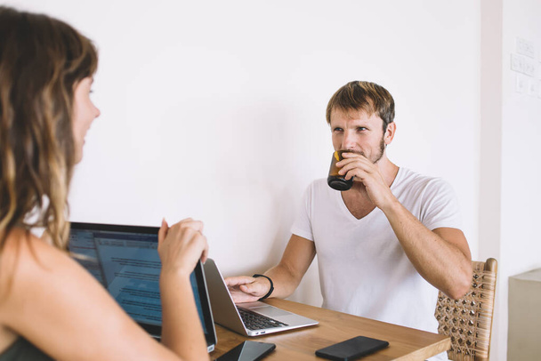 Caucasian male programmer drinking hot tea and communicating with female colleague searching interesting ideas for content website, successful marriage having conversation about network publication - Photo, image