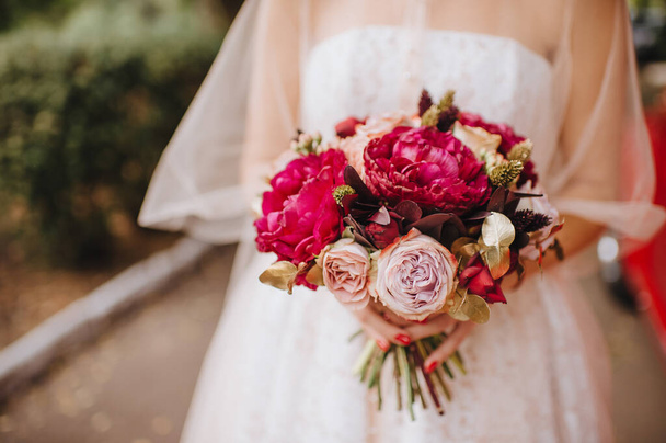 Bride's bouquet close-up, the bouquet consists of red peonies rose. The bride holds the bouquet - Fotografie, Obrázek