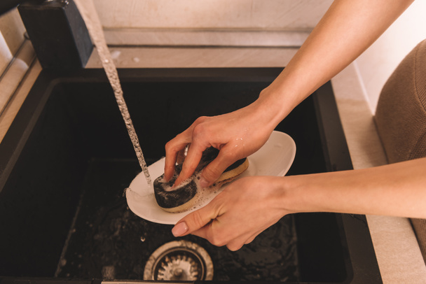 partial view of woman cleaning white plate with sponge - Photo, Image
