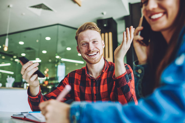 Portrait of cheerful caucasian hipster guy laughing with friend during leisure time in university cafeteria, happy young male and female friends enjoying live communication while studying indoors - Foto, imagen