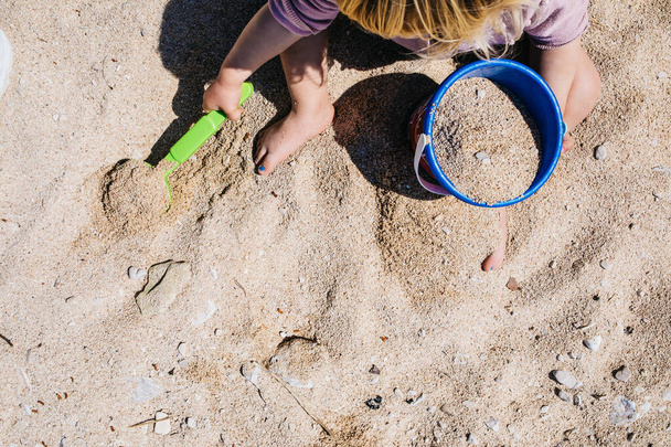 Vaalea kaukasialainen tyttö kaivamassa hiekkaa lapio ja ämpäri rannalla. Kesälomakonsepti. Poika leikkii ja pitää hauskaa. Onnellinen lapsuuden käsite, jossa on tilaa tekstille. Matkustaa lasten kanssa. Huippunäkymä. Yleiskustannukset
 - Valokuva, kuva
