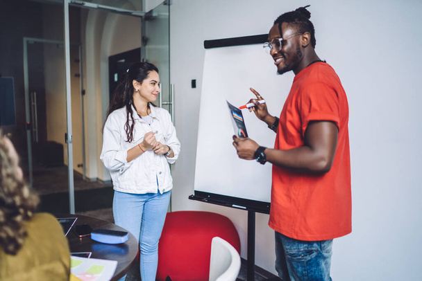 Side view of happy African American man and diverse woman standing in front of whiteboard and talking with students in classroom  - Фото, зображення