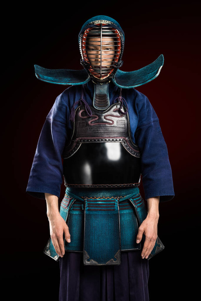 Portrait of man kendo fighter with shinai (bamboo sword). Shot in studio. Isolated with clipping path on dark red background - Foto, afbeelding