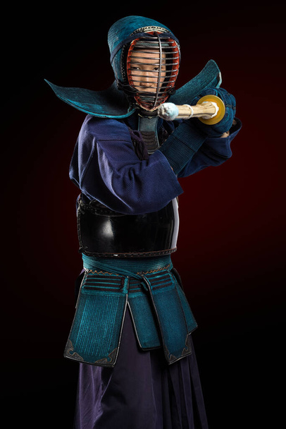 Πορτρέτο του ανθρώπου Kendo μαχητής με shinai (μπαμπού σπαθί). Πυροβολήθηκε στο στούντιο. Απομονωμένο με μονοπάτι αποκοπής σε σκούρο κόκκινο φόντο - Φωτογραφία, εικόνα