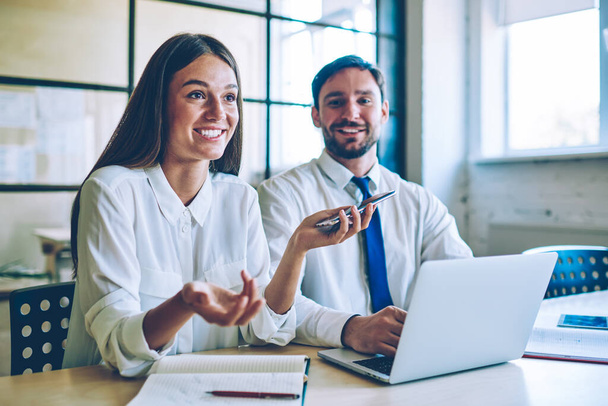 Attractive smiling woman speaking positive history about happening with colleague during break from searching information via modern devices, successful colleagues enjoying friendly entrepreneurship - Foto, imagen