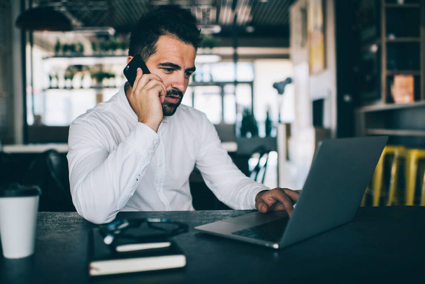 Skilled male entrepreneur reading received email with week schedule information and calling to personal secretary for discussing details, man working remotely with laptop using cell for phoning - 写真・画像