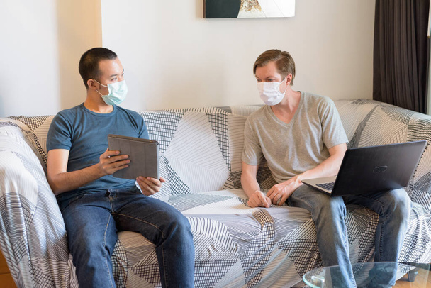 Portrait of young Scandinavian man and young Asian man together with mask in the living room at home under quarantine - Photo, Image