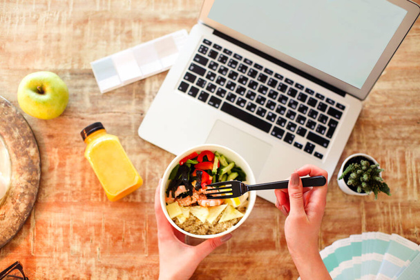 Overhead mujer anónima comiendo plato saludable para el almuerzo sobre la mesa con el ordenador portátil con pantalla vacía
 - Foto, imagen