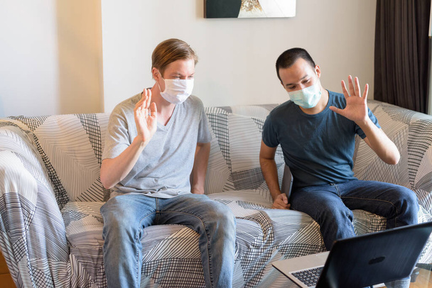 Portrait of young Scandinavian man and young Asian man together with mask in the living room at home under quarantine - Zdjęcie, obraz