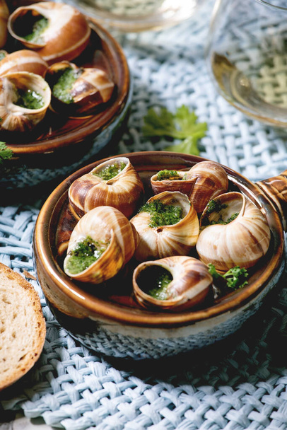 Escargots de Bourgogne - Snails with herbs butter, gourmet dish, in traditional ceramic pan with coriander, bread, glass of white wine on blue straw napkin. Close up - Fotografie, Obrázek