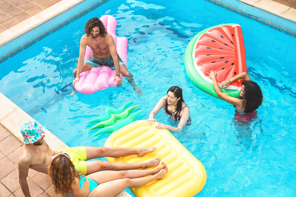 Grupa zadowolonych przyjaciół cieszących się letnim dniem w basenie z nadmuchiwanym - Młodzi wielorasowi ludzie bawiący się w ekskluzywnym hotelu kurortowym - Koncepcja wakacyjnego stylu życia młodzieży - Zdjęcie, obraz