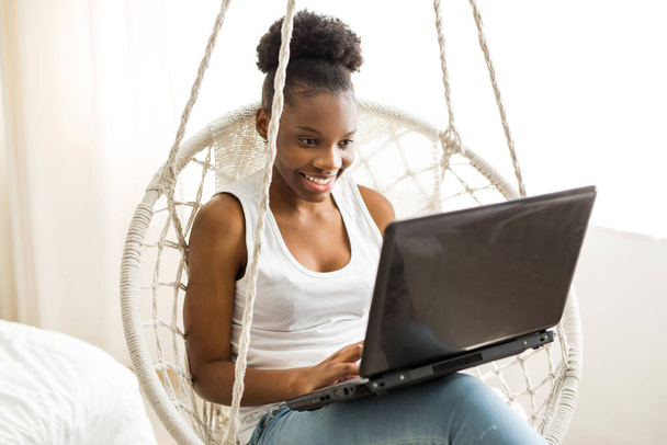 beautiful young african woman sitting in a chair with a laptop - Фото, изображение