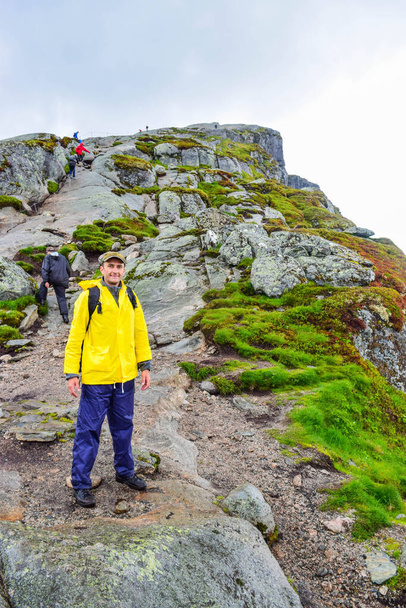 Kjeragboltenへの道の観光客の男。ノルウェーの山々の素晴らしい風景、有名な岩がノルウェーのKjerag山のLysefj ö rdenの上の984メートルの高度で立ち往生. - 写真・画像