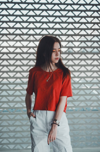 Ritratto di una ragazza elegante e alla moda nel parcheggio. Ragazza in una t-shirt rossa e pantaloni bianchi
. - Foto, immagini