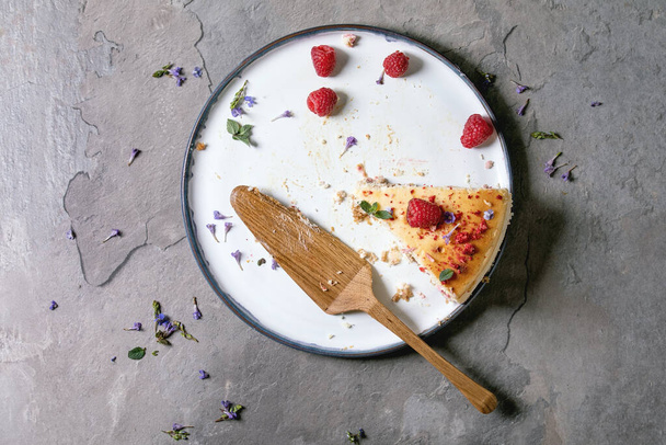Last piece of homemade raspberry baked cheesecake on plate decorated by fresh raspberries and mint, with wooden cake server over grey textute background. Flat lay, space - Fotografie, Obrázek