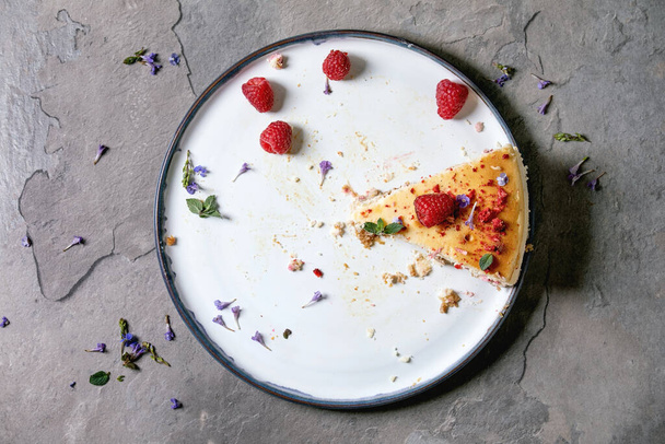 Last piece of homemade raspberry baked cheesecake on plate decorated by fresh raspberries and mint over grey textute background. Flat lay, space - Foto, imagen