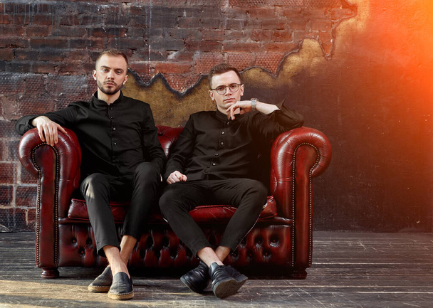 Dos jóvenes empresarios están sentados en un sofá de cuero rojo en el estudio. Jóvenes emprendedores, generación futura. El espíritu de independencia. Puesta en marcha
 - Foto, imagen
