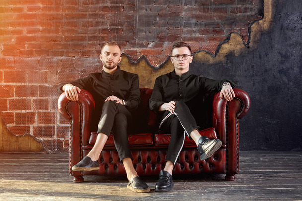 Два молодых бизнесмена сидят на красном кожаном диване в студии. Молодые предприниматели, будущее поколение. Дух независимости. Запуск
 - Фото, изображение