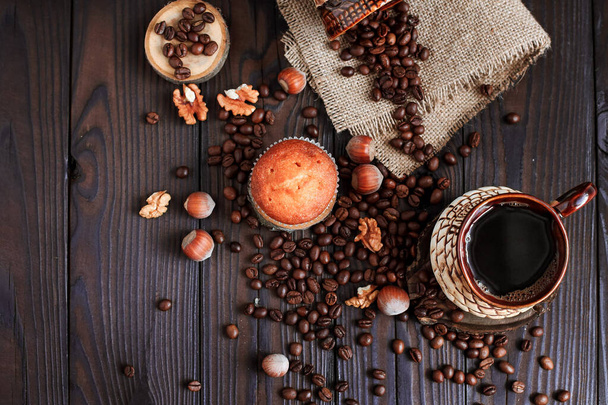 hot fragrant coffee in a vintage clay cup and coffee beans with nuts on a dark wooden background - Photo, Image